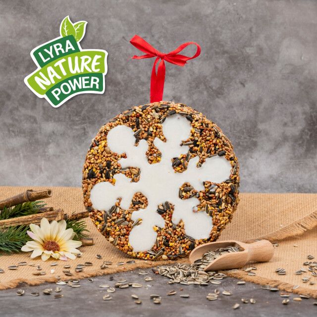 Runder Vogelkuchen mit Schneeflockenmuster. Logo: Lyra Nature Power. Rotes Band. Samen und Zubehör.