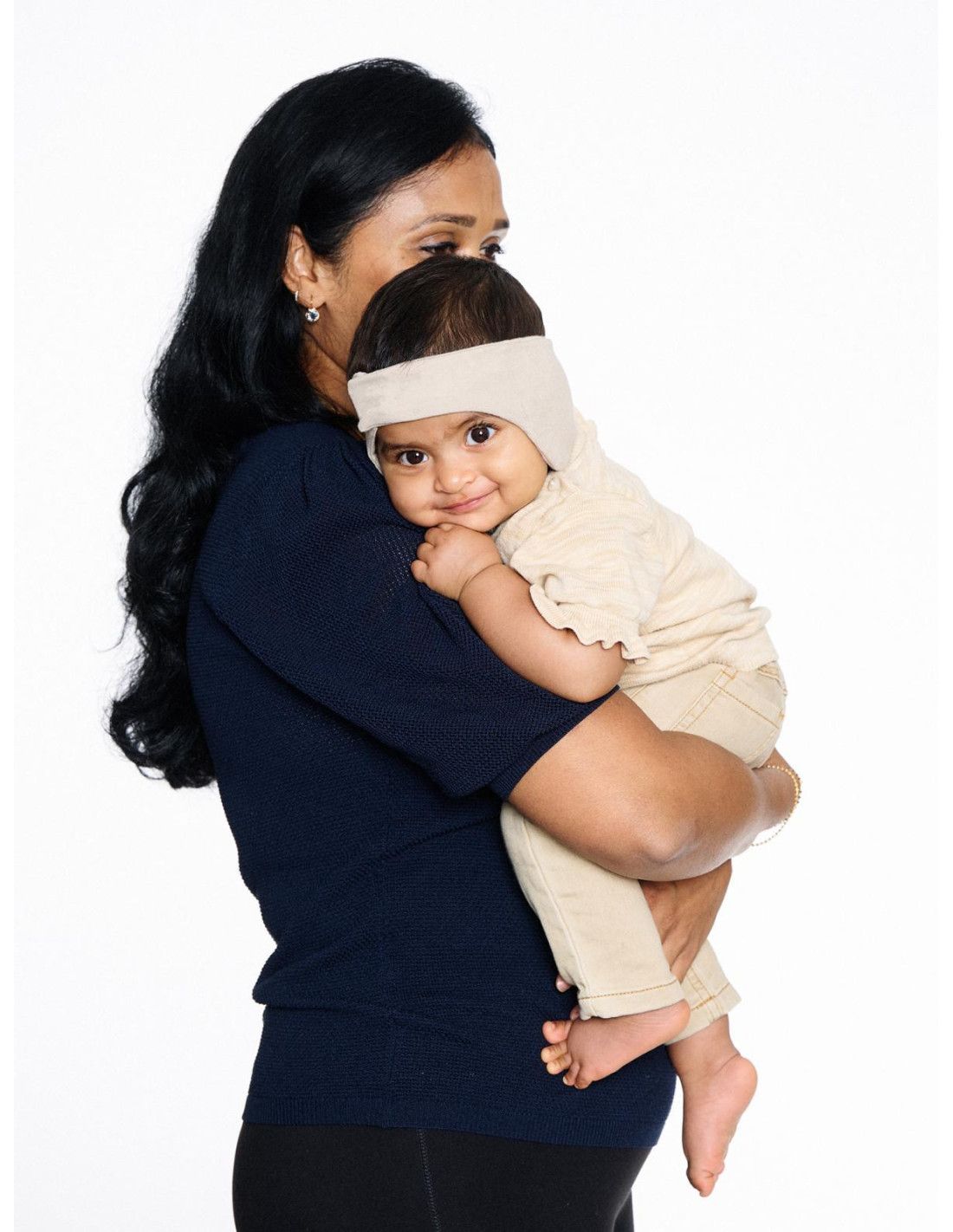 Beige Kopfbedeckung für Babys, die über die Ohren reicht.