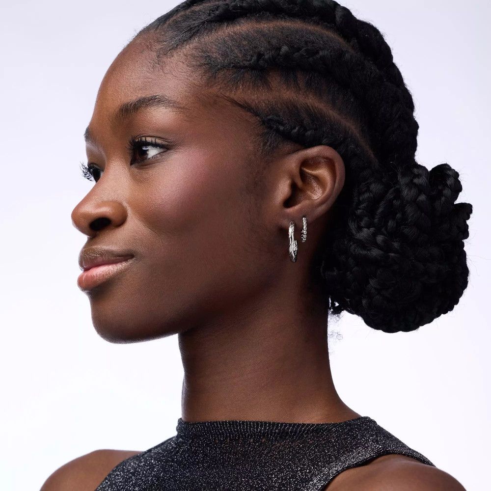 Profil einer Frau mit Zopf und Ohrringen. Aufgetragenes Rouge auf den Wangen. Helle Haut, dunkle Haare.