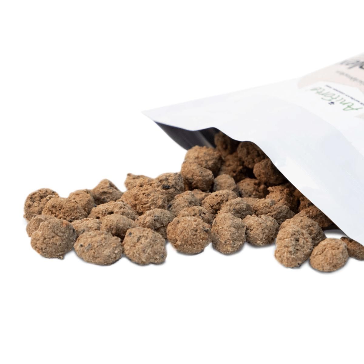 Geöffnete Tüte mit braunen, runden Snacks. Snacks liegen verstreut auf weißem Untergrund. Produktname teilweise sichtbar.