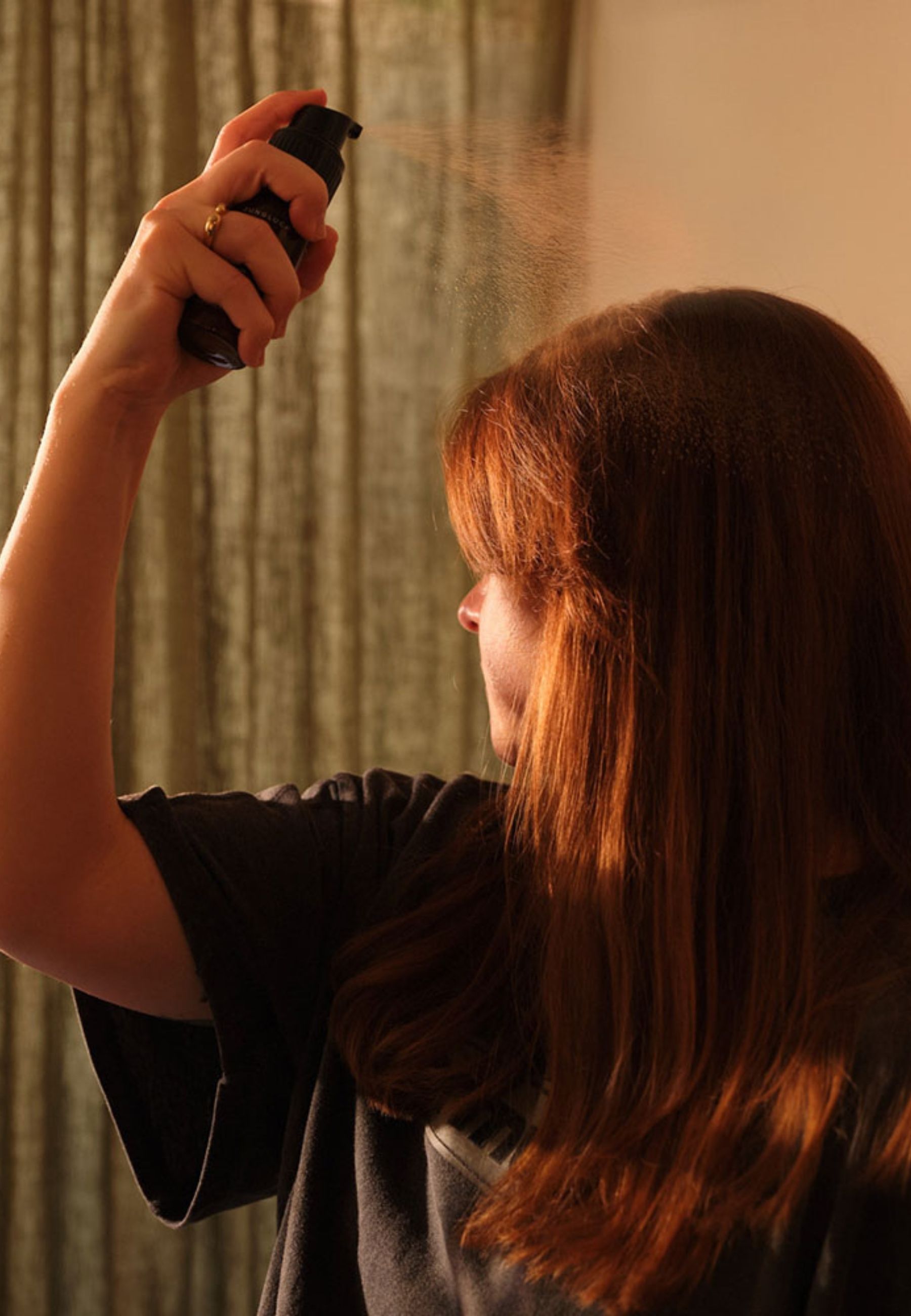 Person sprüht Trockenshampoo in die Haare. Schwarze Flasche, rotes Spray.