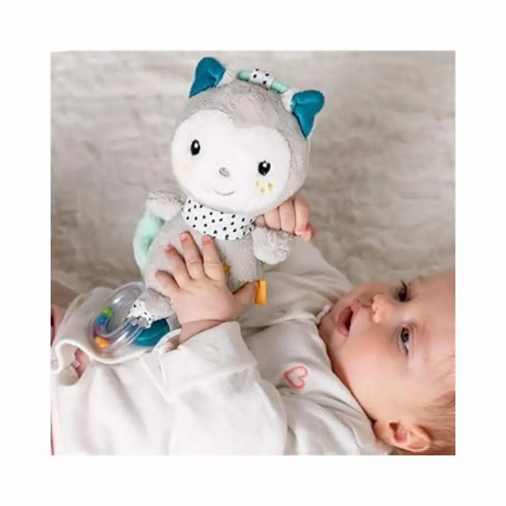 Baby hält graues Kuscheltier mit blauen Ohren und gepunktetem Schal. Mit Stern, Spiegel und Rassel. Liegt auf weißem Untergrund.