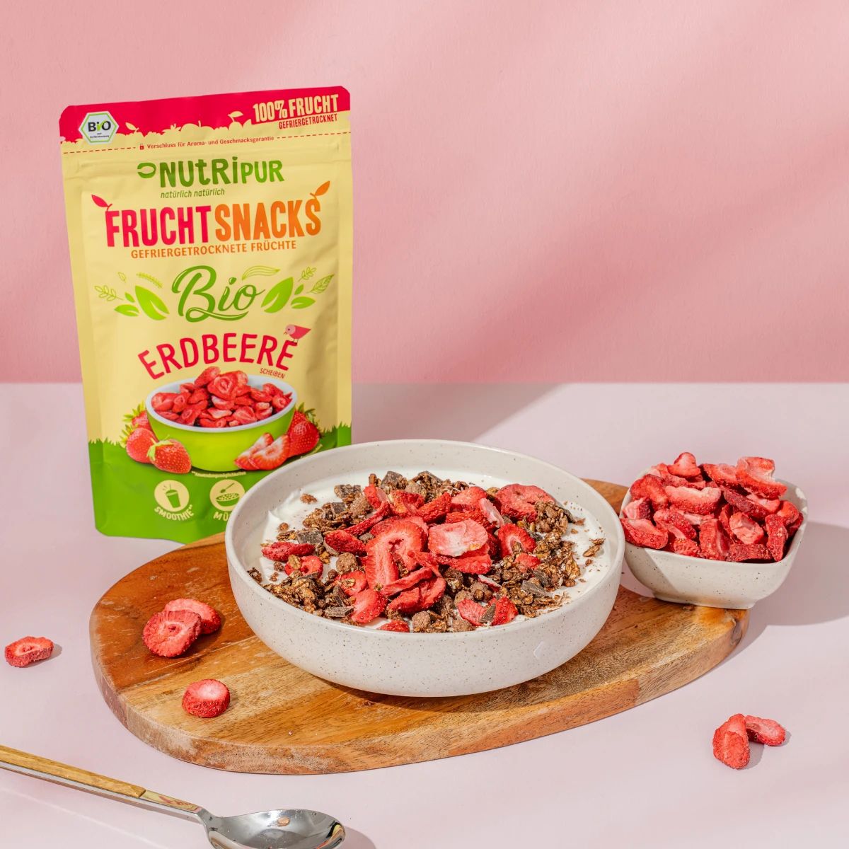 Beutel mit gefriergetrockneten Erdbeeren. Aufschrift: NutriPur, Bio, Frucht Snacks, 100% Frucht. Erdbeeren in Schalen, auf Holzbrett.