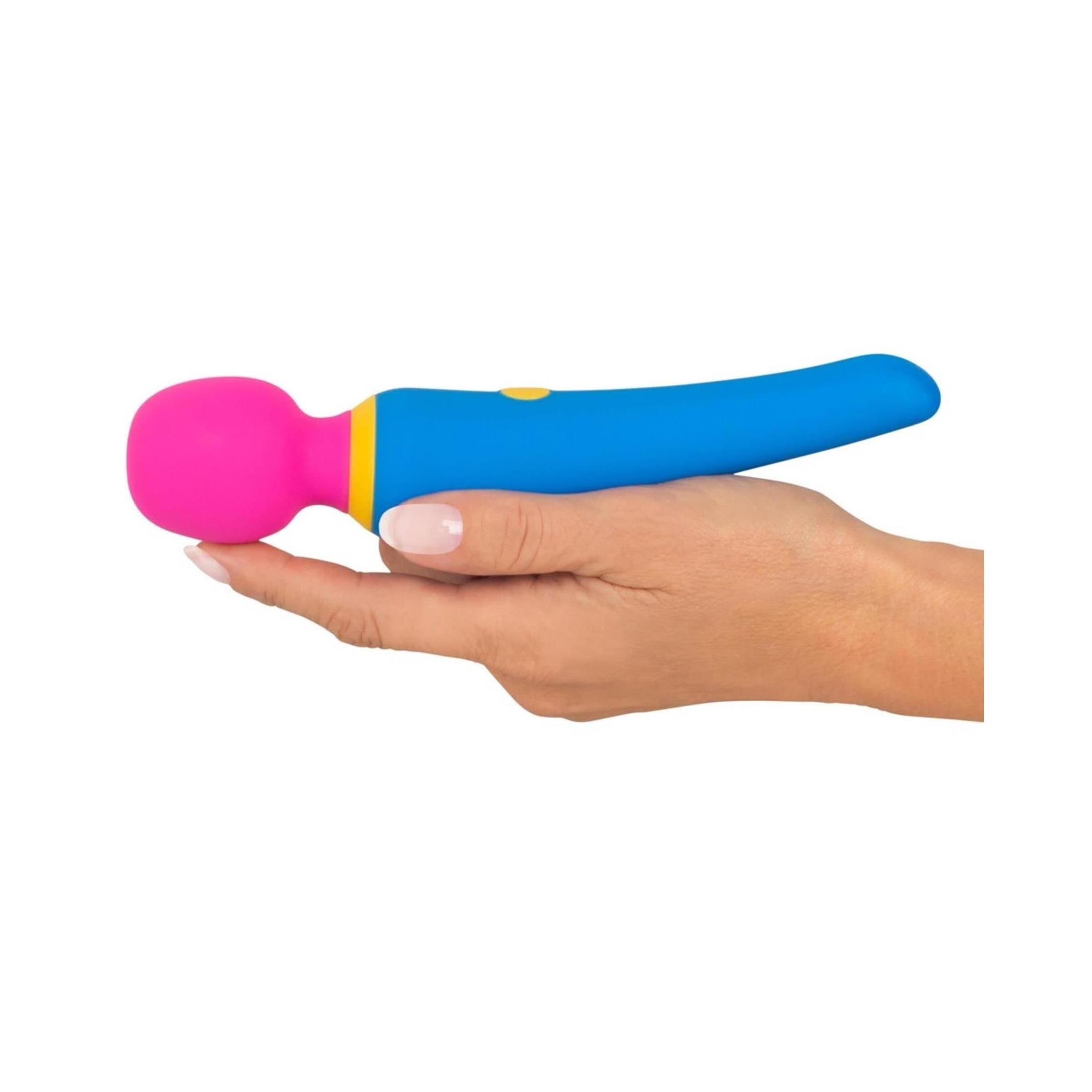 Hand hält einen blau-gelb-pinkfarbenen Vibrator. Zylindrischer Griff, runder Kopf. Gelber Knopf.
