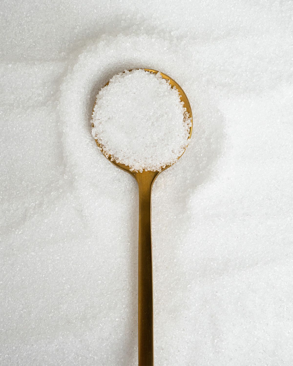 Goldener Löffel mit weißem Xylit-Kristallzucker, auf einem Haufen Xylit.