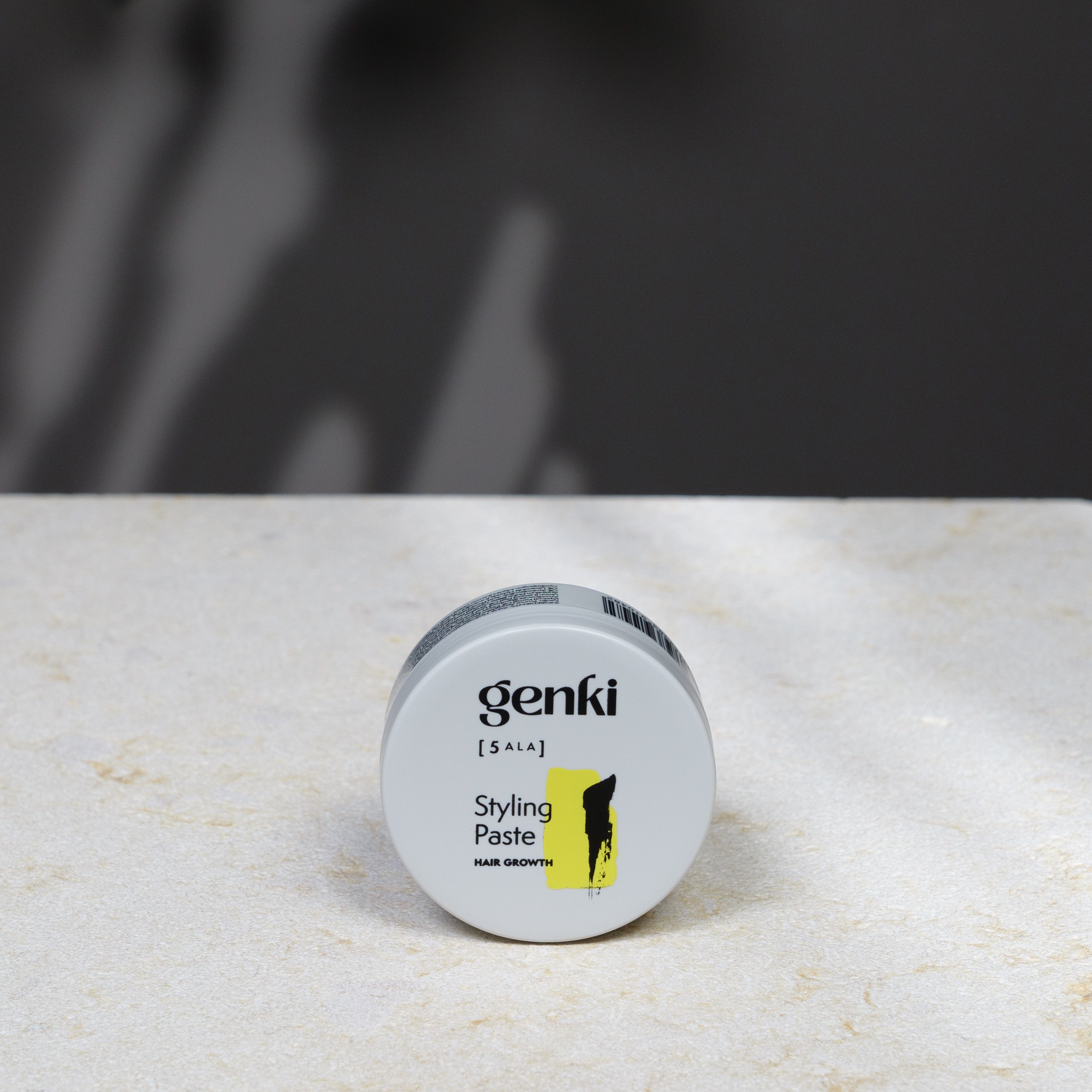 Runde, graue Dose mit Genki [5 ALA] Styling Paste. Gelber Farbfleck, schwarze Schrift.
