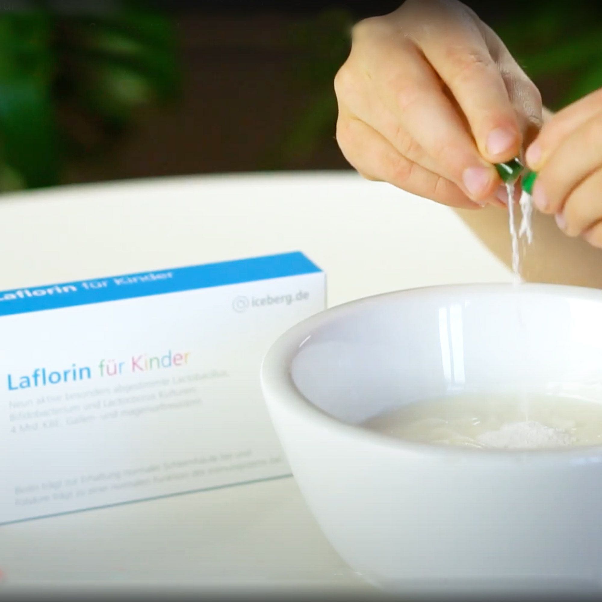 Kind öffnet Kapsel über einer Schüssel. Daneben: Packung Laflorin für Kinder. Inhalt wird in Schüssel gegeben.