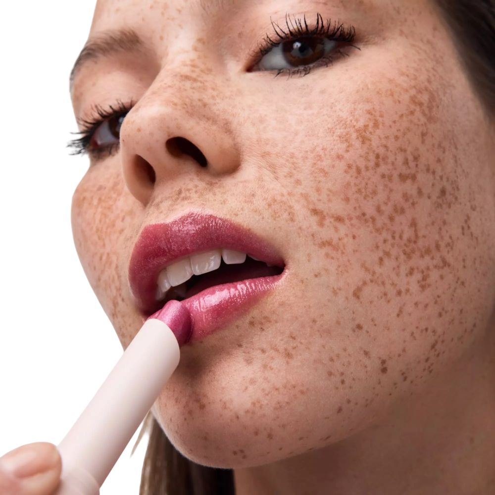 Nahaufnahme einer Frau mit Sommersprossen, die sich Lippenstift aufträgt.