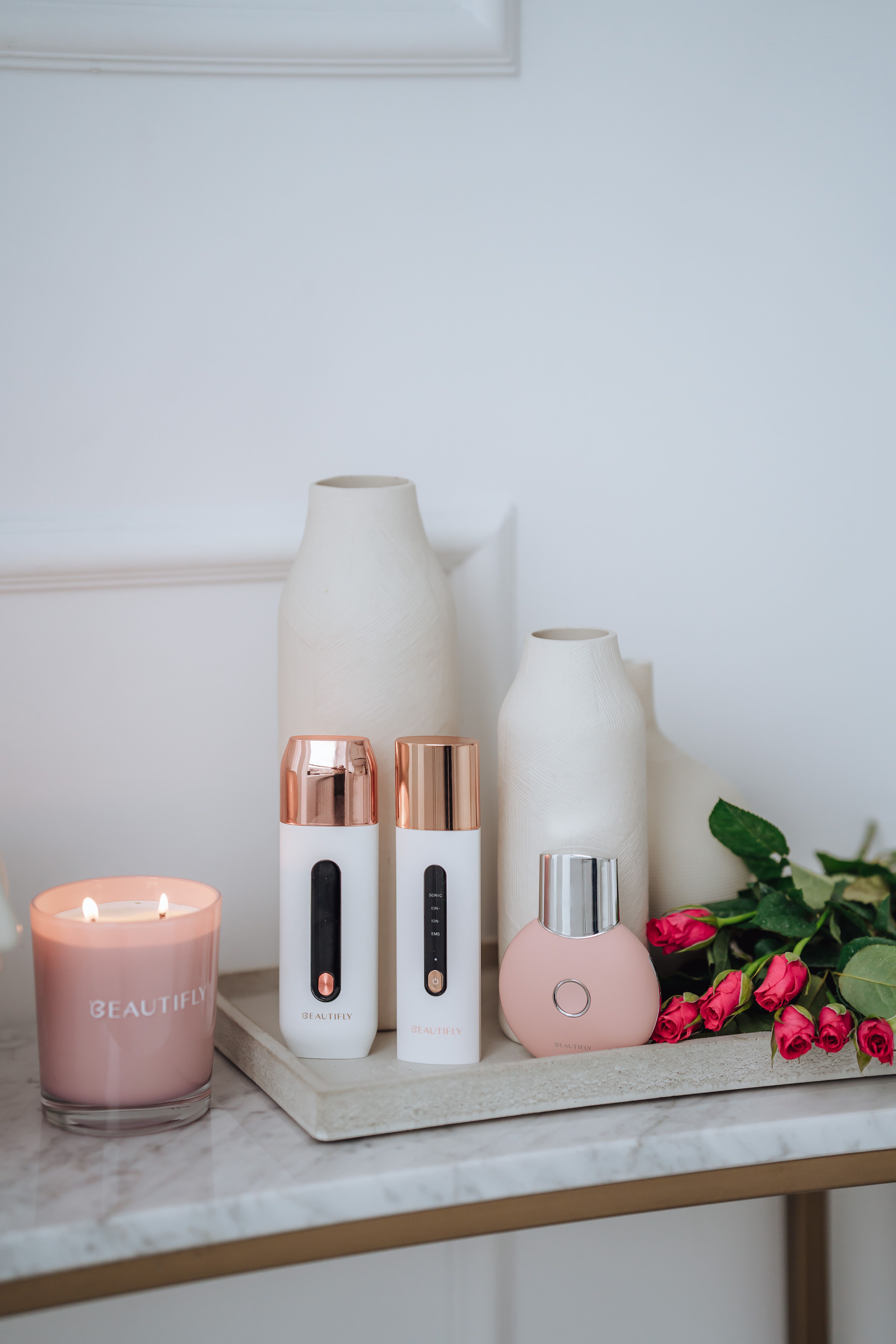 Stillleben mit BEAUTIFLY B-Scrub Pro Slim Ultraschall Peeling, Kerze, Vase und Blumen auf einem Tablett.