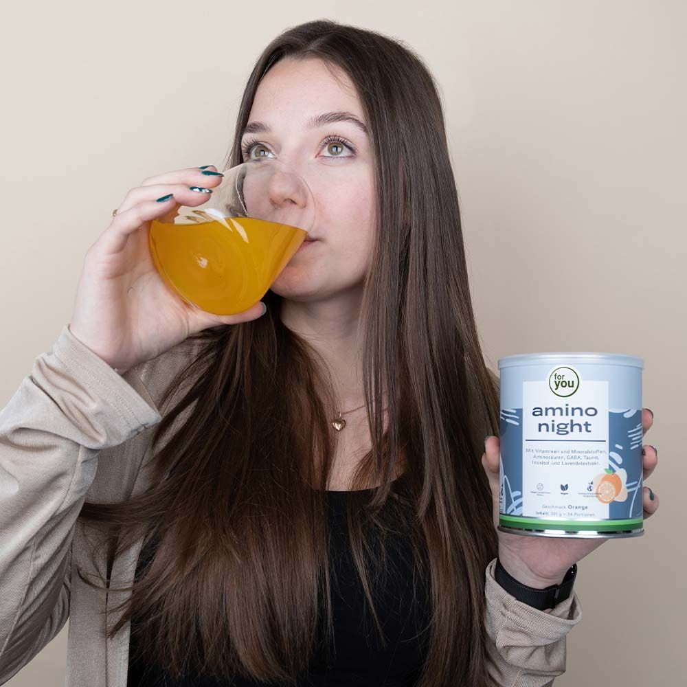 Frau trinkt aus einem Glas. In der Hand hält sie eine Dose mit "for you amino night". Aufdruck: Vitamine, Mineralstoffe, Aminosäuren, GABA, Taurin, Inositol und Lavendelextrakt.
