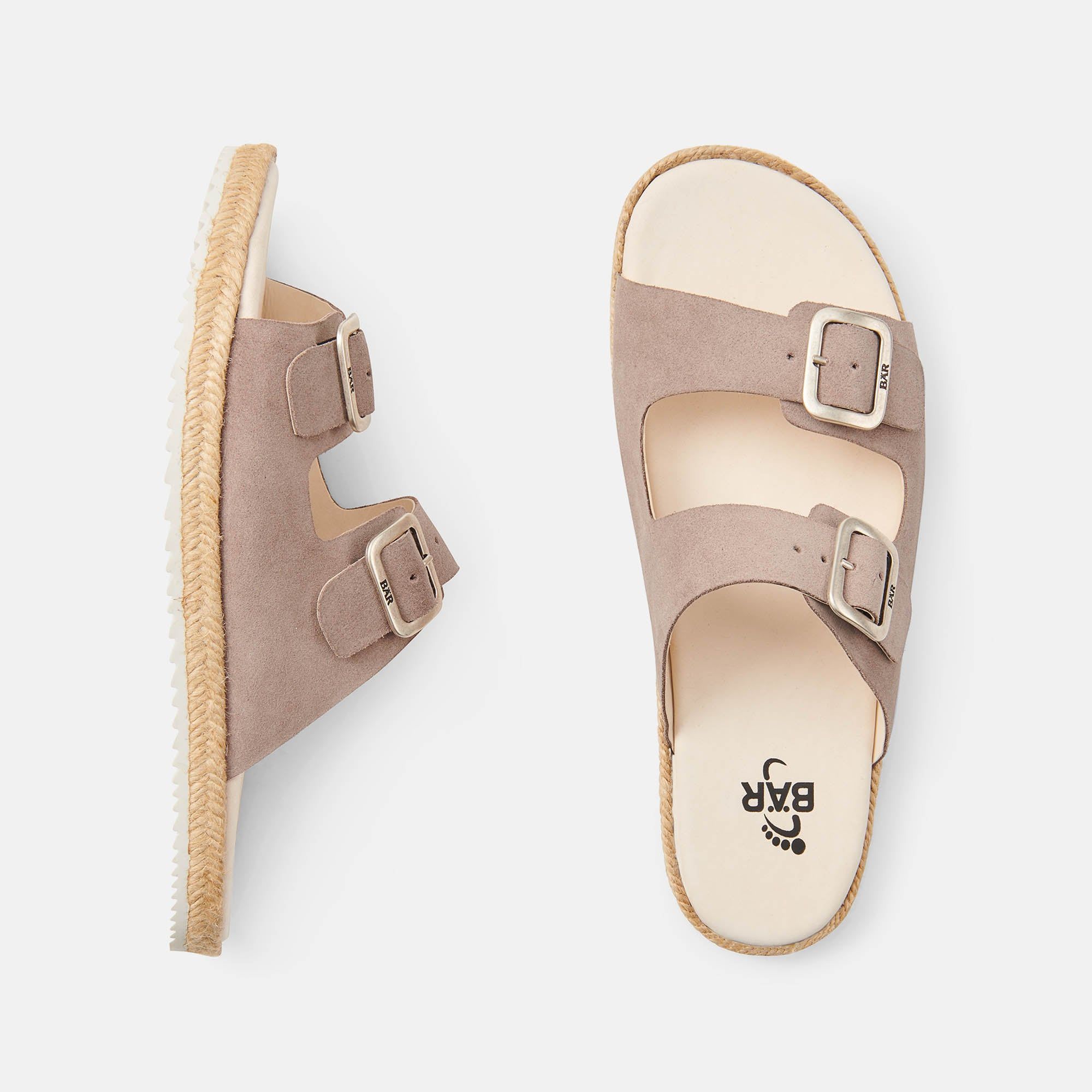 Zwei Pantoletten, eine von oben, eine von der Seite. Beige mit zwei Schnallen. Sohle weiß, Rand geflochten. BAR auf Riemen.