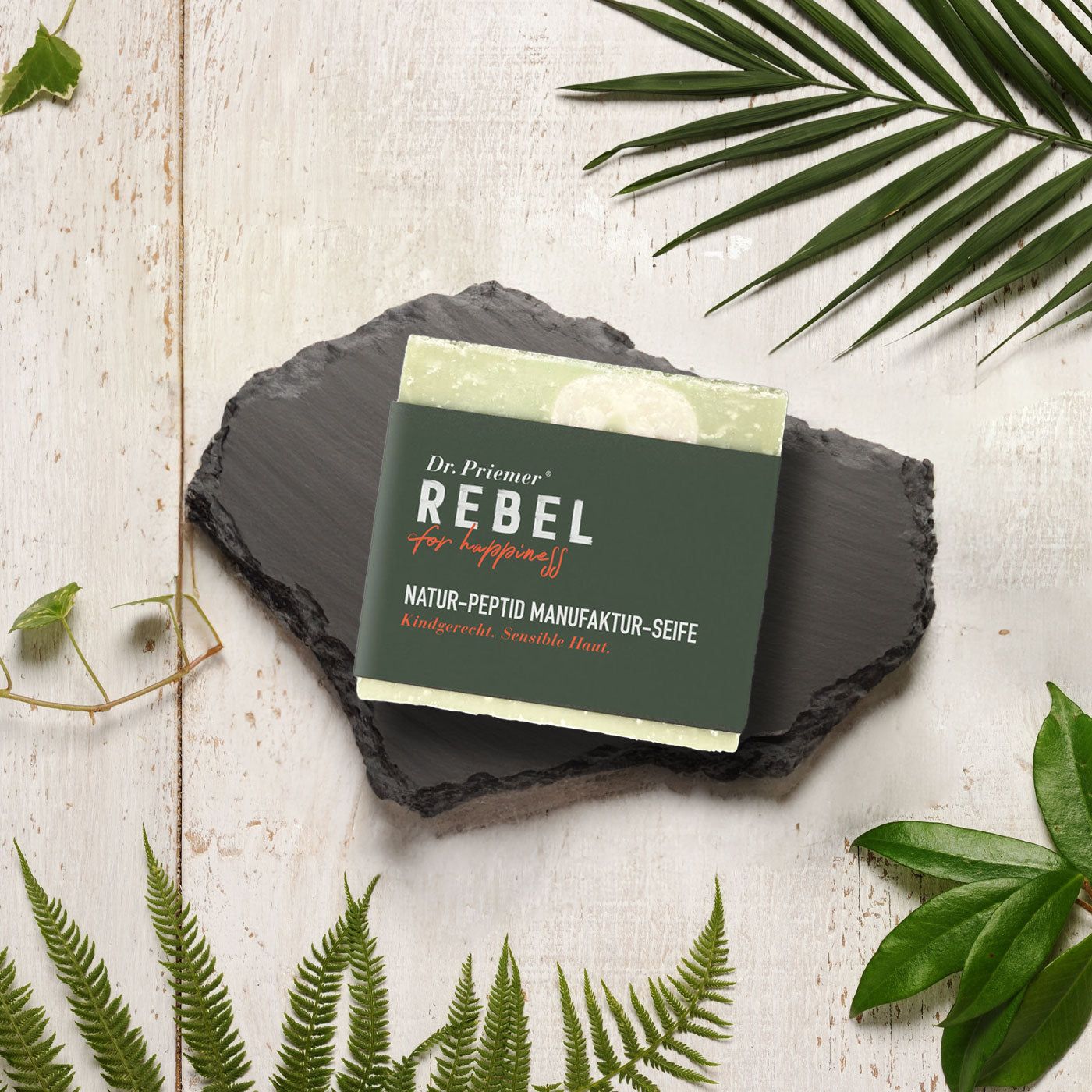 Seife auf Schieferplatte, umgeben von Blättern. Aufschrift: Dr. Priemer, REBEL for happiness, Natur-Peptid Manufaktur-Seife.