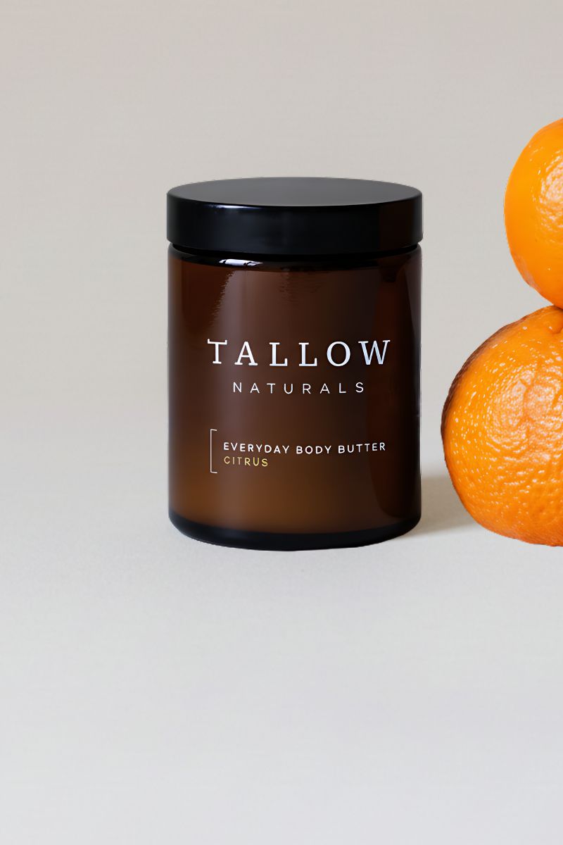 Braune Glasdose mit schwarzem Deckel. Aufschrift: TALLOW NATURALS, EVERYDAY BODY BUTTER CITRUS. Daneben Orangen.