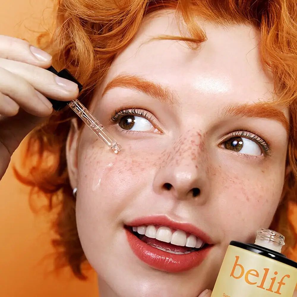 Frau mit Sommersprossen trägt Serum mit Pipette auf.
