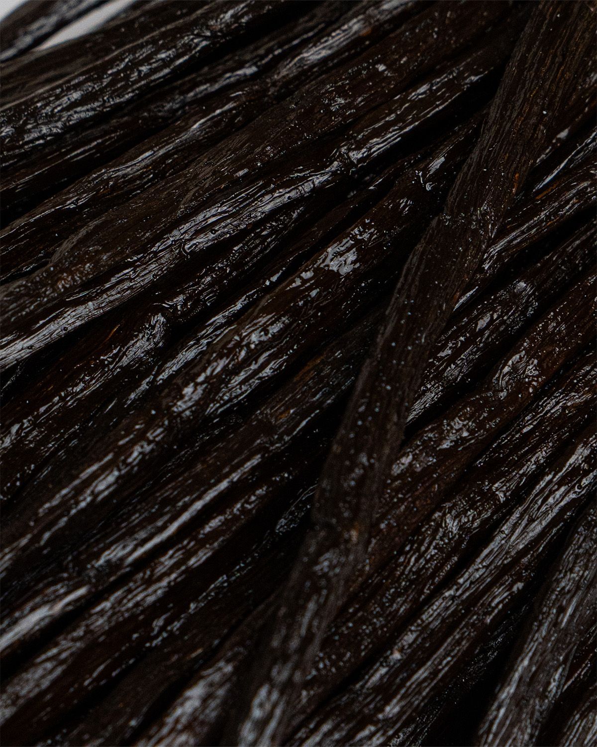 Nahaufnahme von vielen dunklen Vanilleschoten. Längliche Form, dunkelbraune Farbe, leicht glänzend.