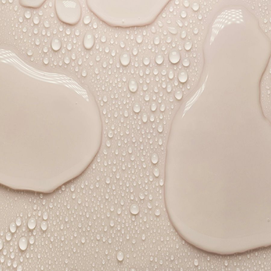 Nahaufnahme von hellrosa Flüssigkeitstropfen mit Wassertropfen auf hellem Hintergrund.