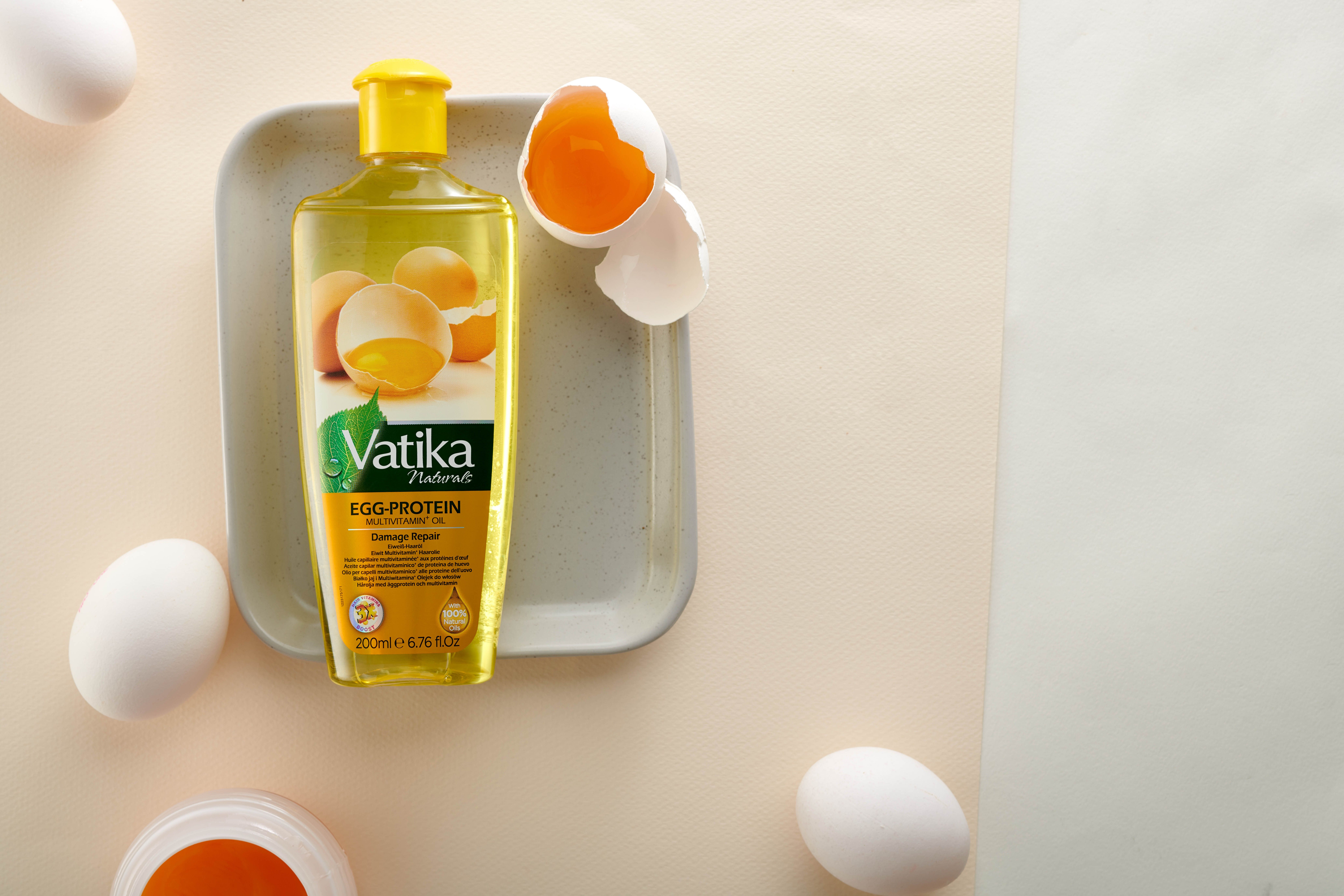 Haarölflasche auf einem Tablett, umgeben von Eiern. Aufschrift: Vatika Egg-Protein Multivitamin Oil. Mit Ei-Abbildung.