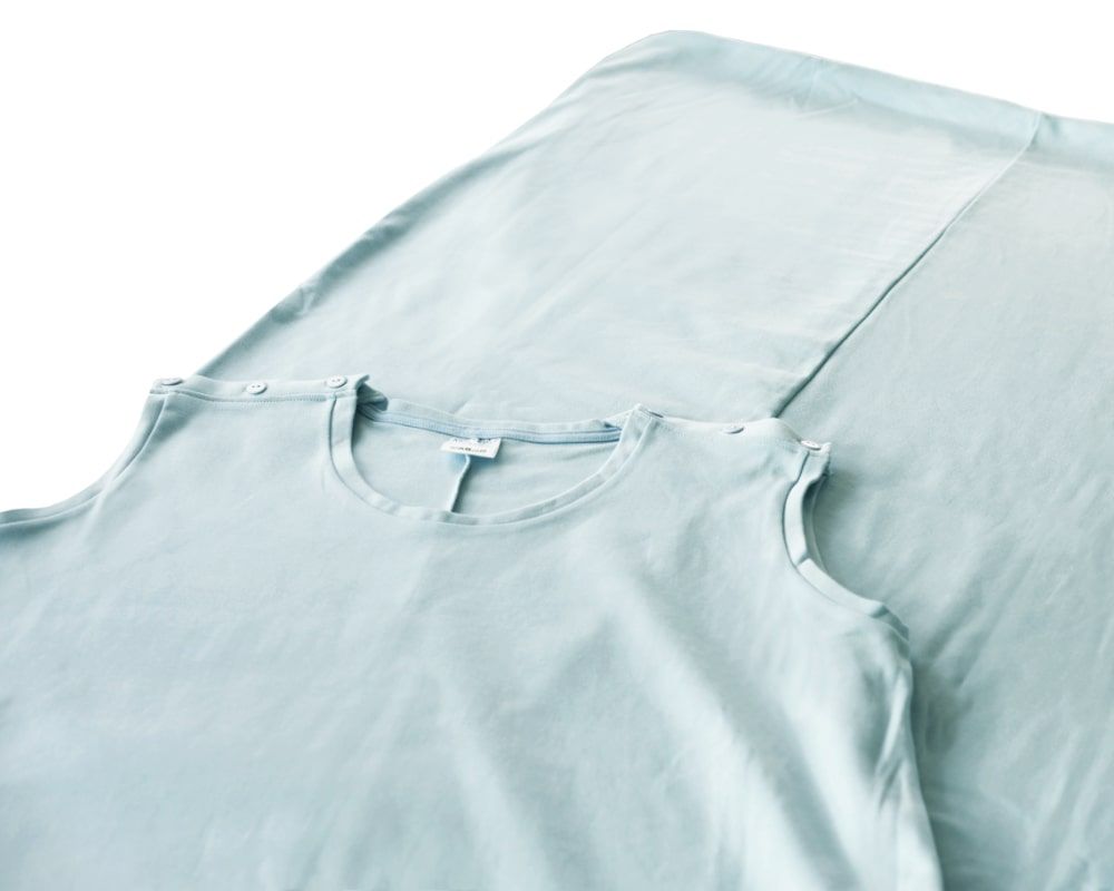 Hellblauer Pflegeschlafsack mit Knopfleiste an den Schultern. Rundhalsausschnitt. Stoff. Liegend.