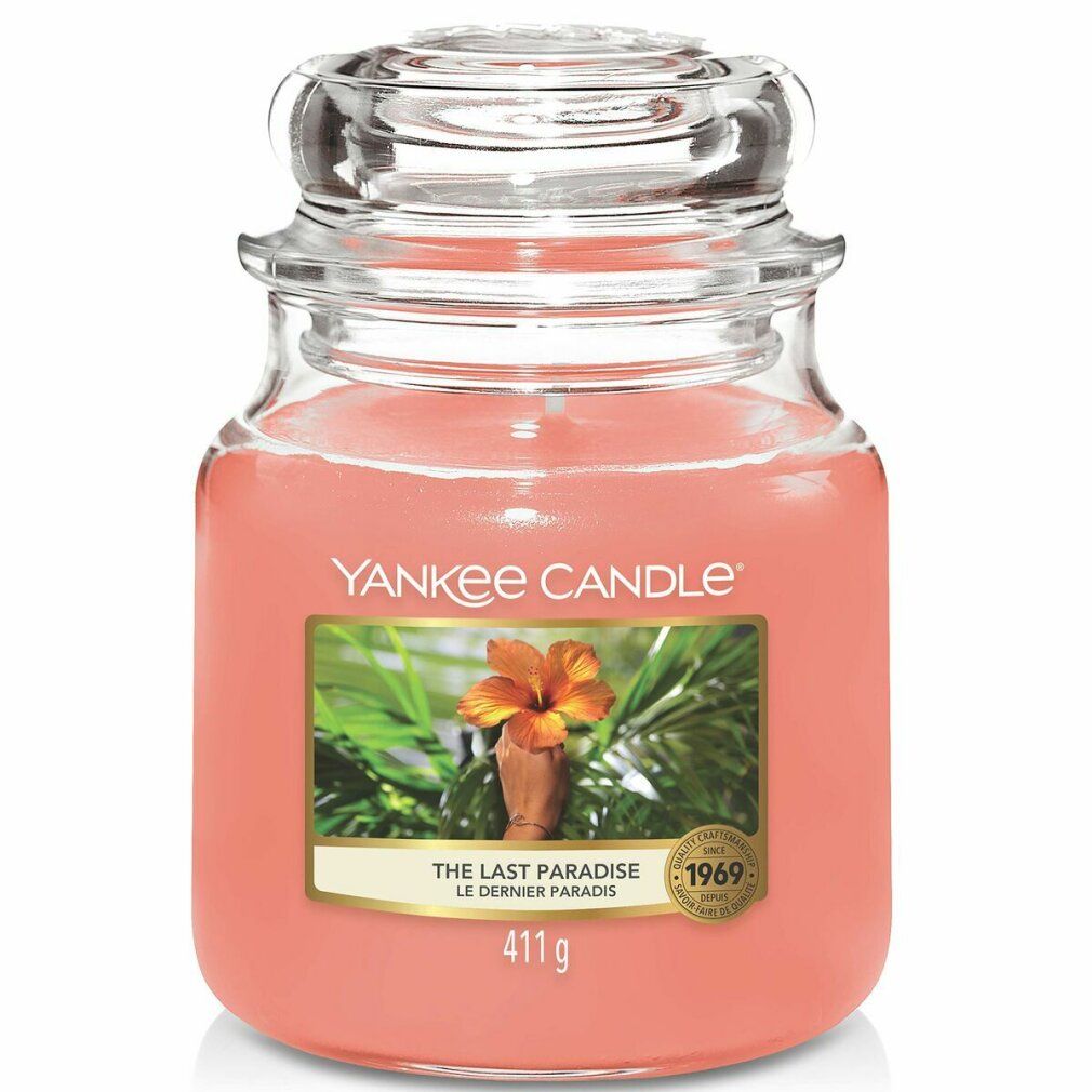 Yankee Candle Duftkerze, Medium, The Last Paradise. Rosa Wachs in Glasbehälter mit Deckel. Etikett mit Blüte und Text.