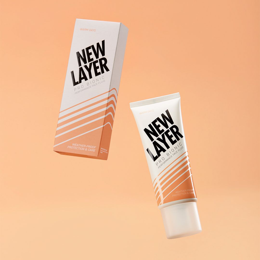 Gesichtsfluid-Tube und Karton. Weiß, orangefarbene Streifen und schwarzer Schriftzug: NEW LAYER Pro Bionic Performance Face Fluid. Schwebende Darstellung.