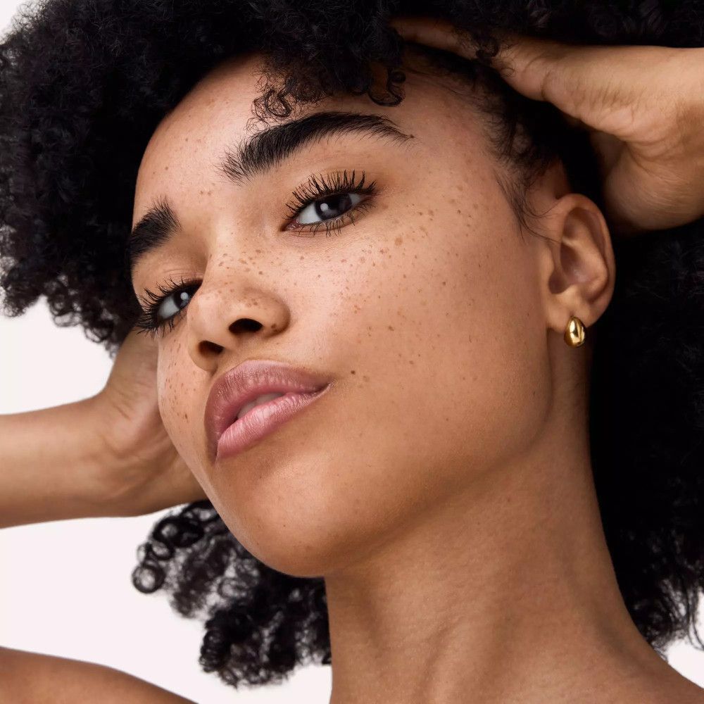 Porträt einer Frau mit Sommersprossen. Geschminkte Augen mit Mascara. Goldene Ohrringe.