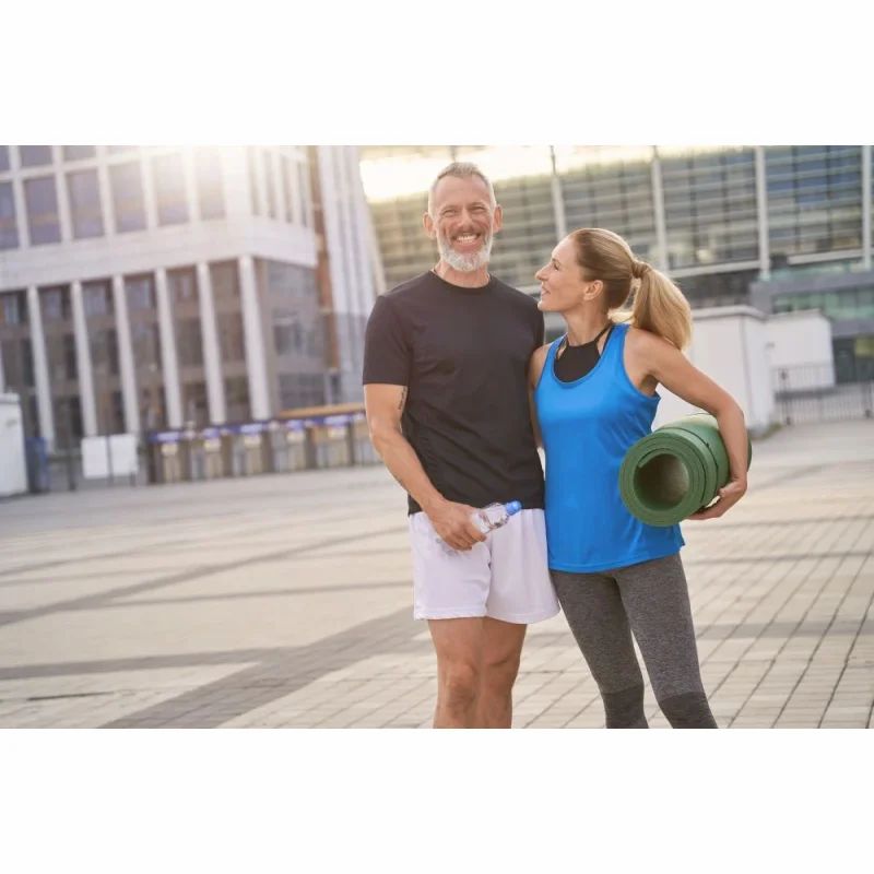 Ein Mann und eine Frau stehen im Freien. Die Frau hält eine Yogamatte.