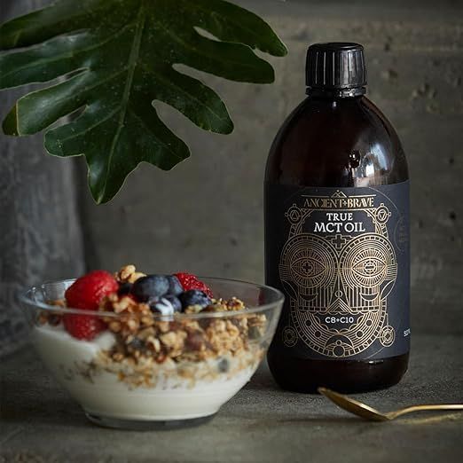 Eine Schale mit Joghurt, Müsli und Beeren steht neben einer Flasche MCT-Öl. Ein goldenes Löffelchen liegt daneben.