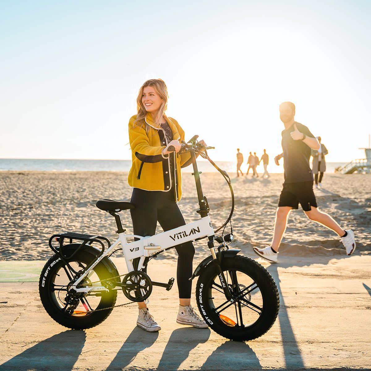 Weißes, zusammenklappbares E-Bike mit schwarzen Reifen. Frau steht daneben. Vitilan V3 auf dem Rahmen.