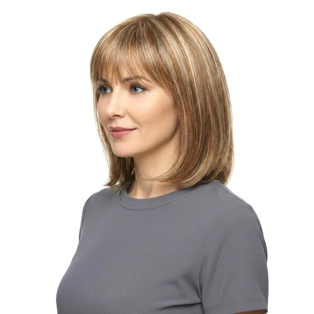Perücke Mola von trendhair. Blond-braune Haarfarbe mit Pony. Mittellange, gestufte Frisur. Frau trägt graues Oberteil.