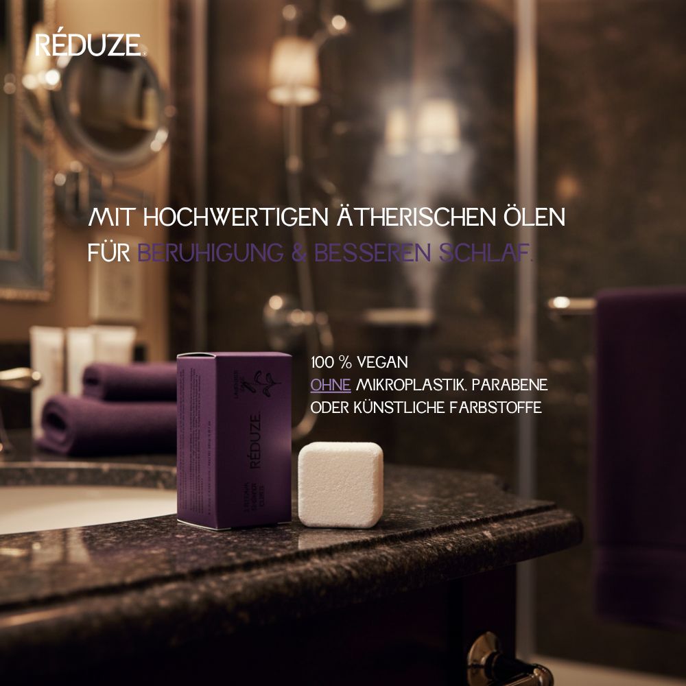 Lila Schachtel und weißer Duschwürfel auf einer dunklen Oberfläche. Text: RÉDUZE.