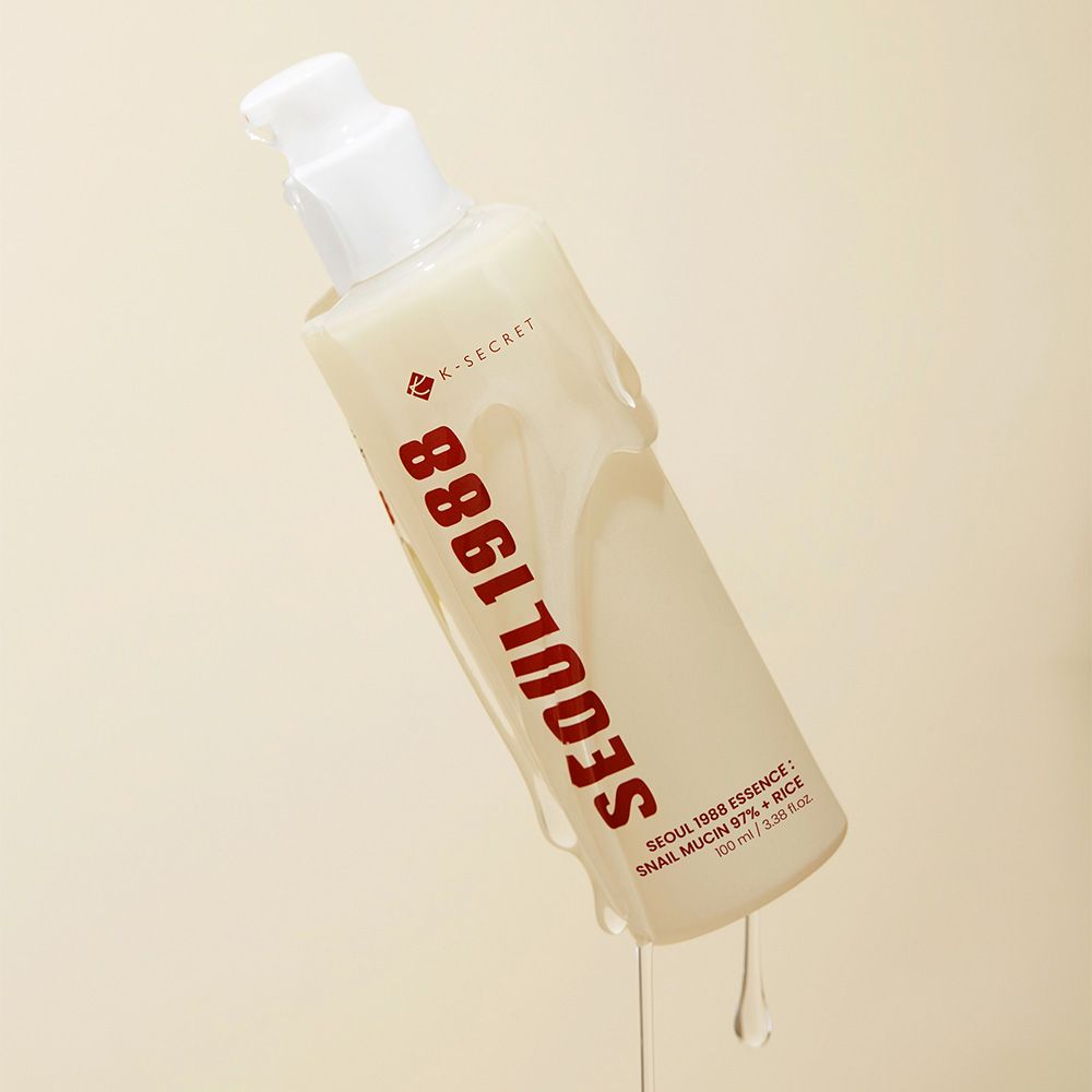 K-SECRET Seoul 1988 Essence Flakon kippt, klares Serum tropft herab. Beige Flasche mit rotem Schriftzug.