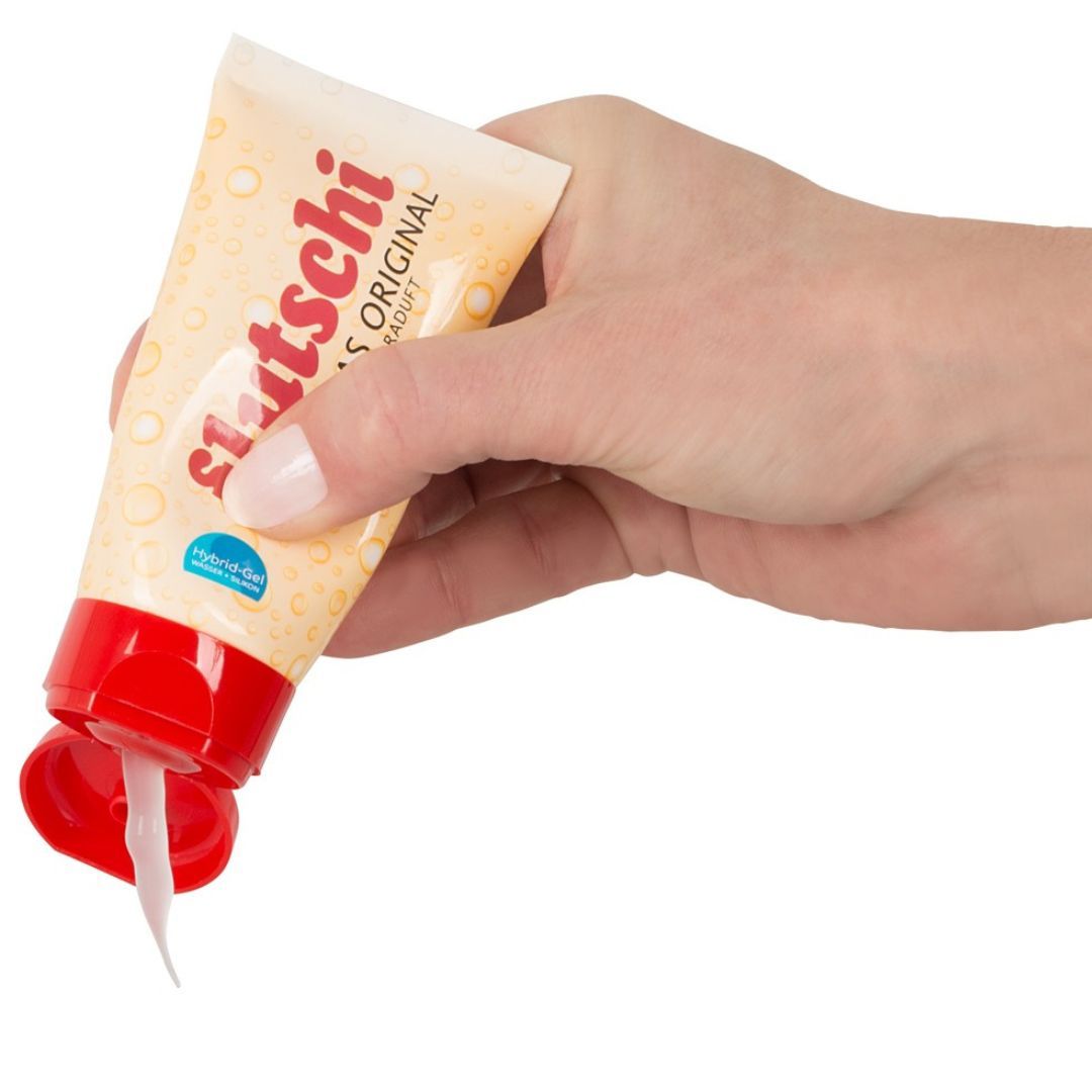 Hand hält Tube 'Flutschi - das Original'. Gel fließt aus der Öffnung. Roter Deckel. Beige Tube.