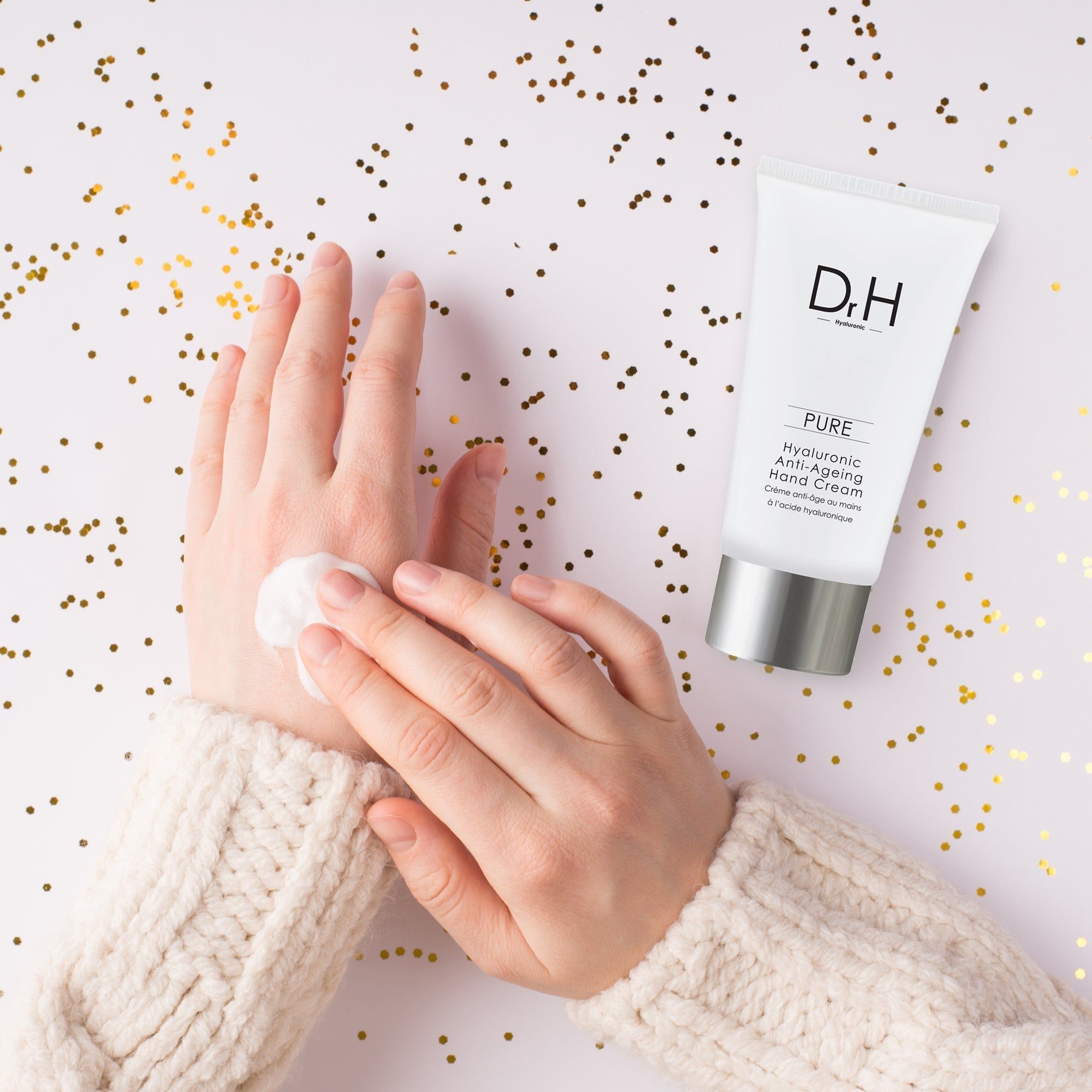 Hände mit Creme. Tube daneben. Aufschrift: Dr. H, Pure, Hyaluronsäure Anti-Aging Handcreme. Goldkonfetti.