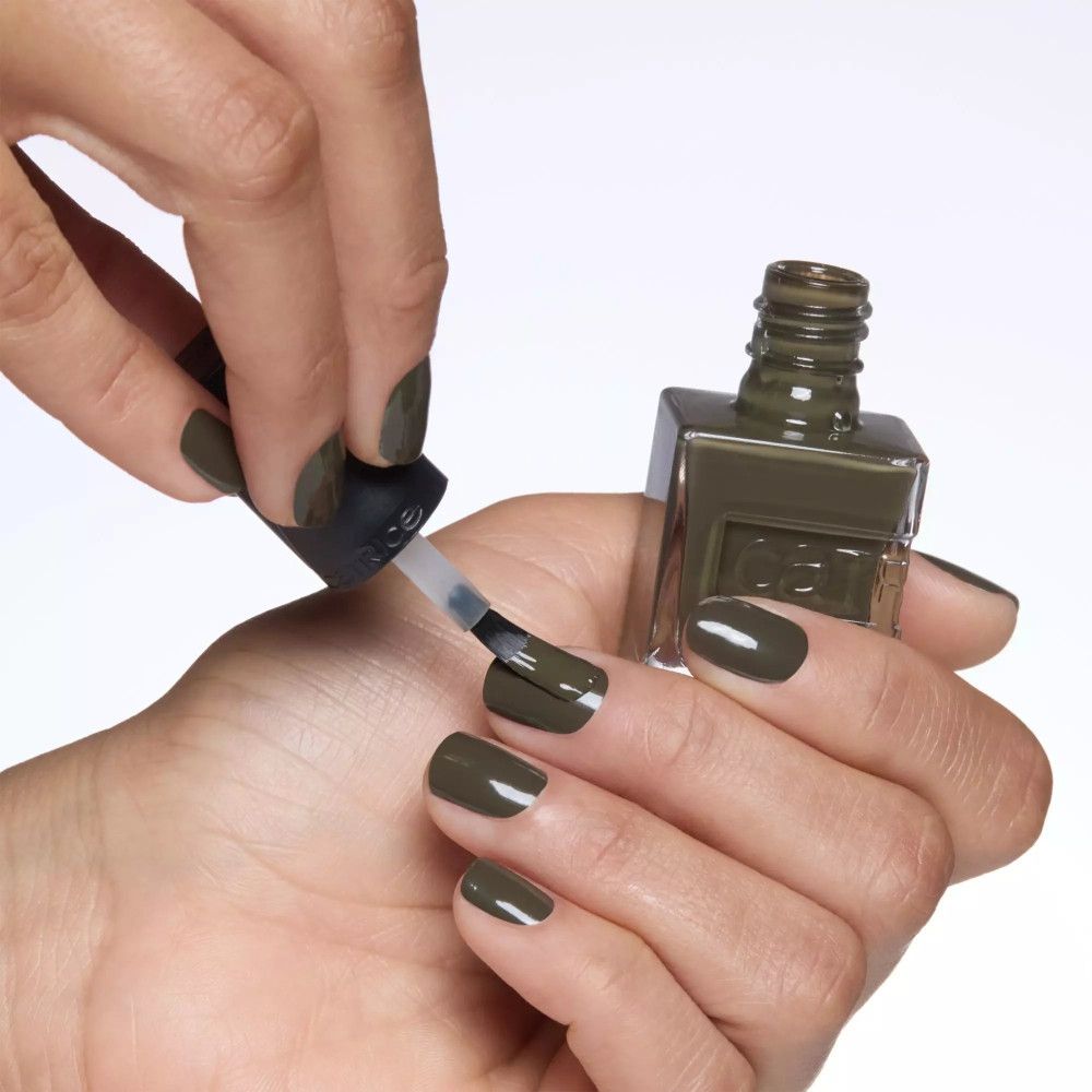 Hand lackiert Nägel mit olivgrünem Nagellack. Eine Nagellackflasche und ein Pinsel sind sichtbar.