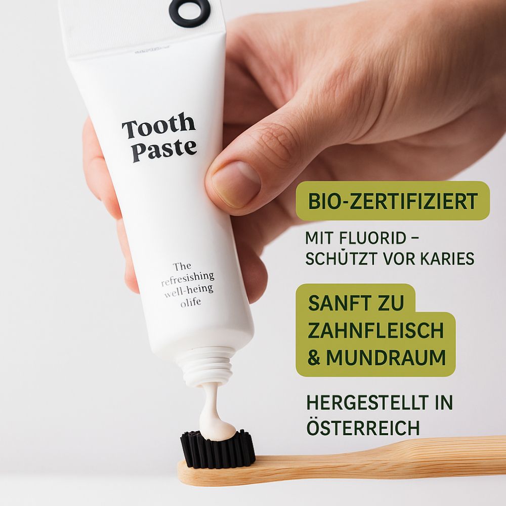 Weiße Zahnpasta-Tube mit schwarzem Verschluss. Aufschrift "Tooth Paste". Auf einer Zahnbürste wird Zahnpasta aufgetragen. Text: Bio-zertifiziert, sanft zum Zahnfleisch.