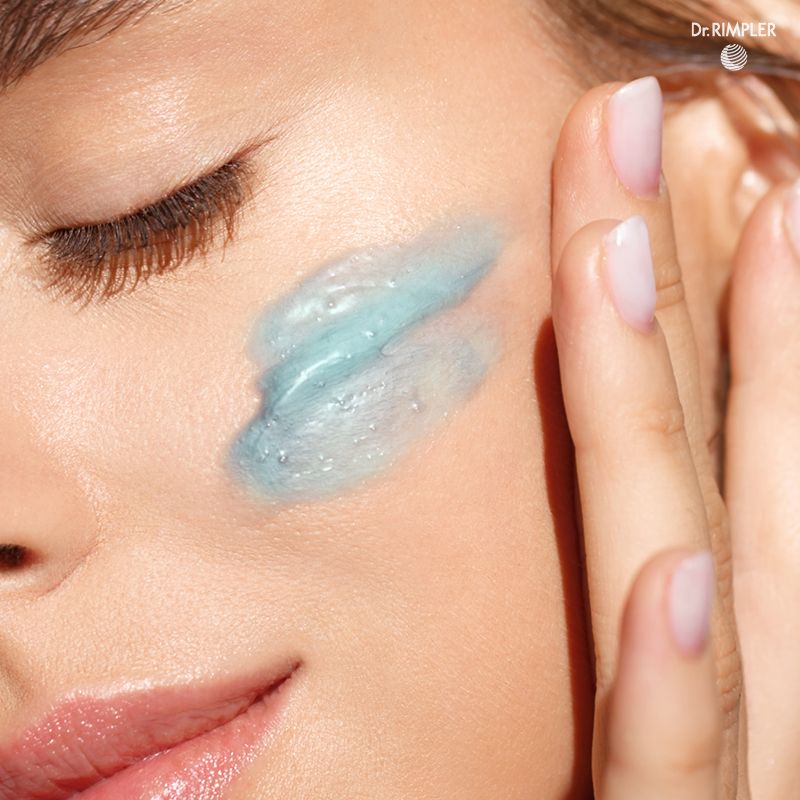 Nahaufnahme einer Frau, die Gel auf ihr Gesicht aufträgt. Das Gel ist hellblau.