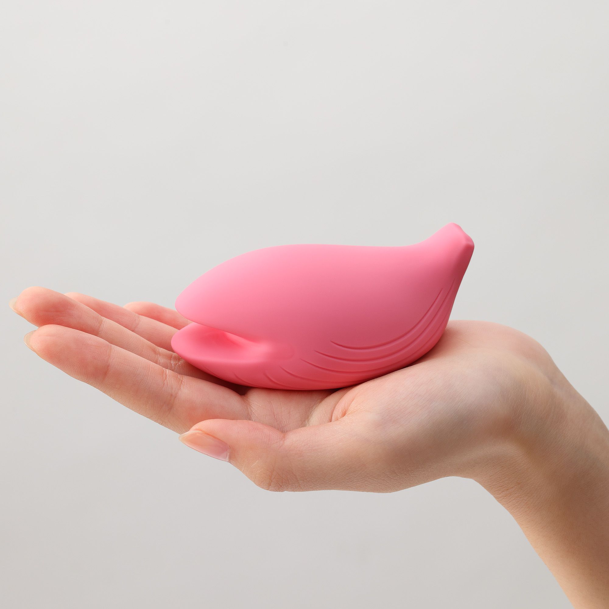 Rosa Vibrator in Hand gehalten. Organische Form mit geriffelter Oberfläche und Öffnung. Auf heller Haut.