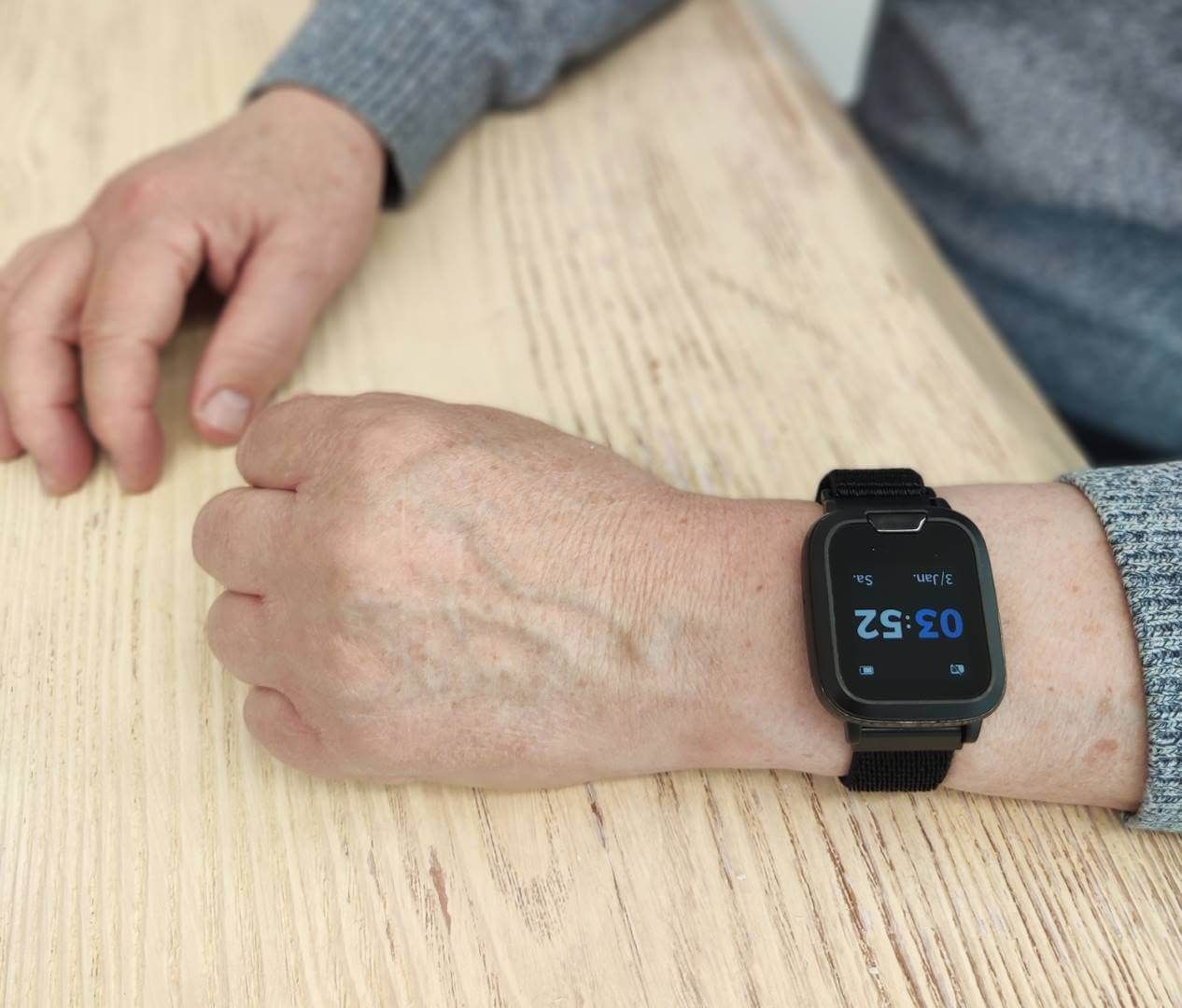 Schwarze Smartwatch am Handgelenk eines älteren Mannes, zeigt digitale Uhrzeit.