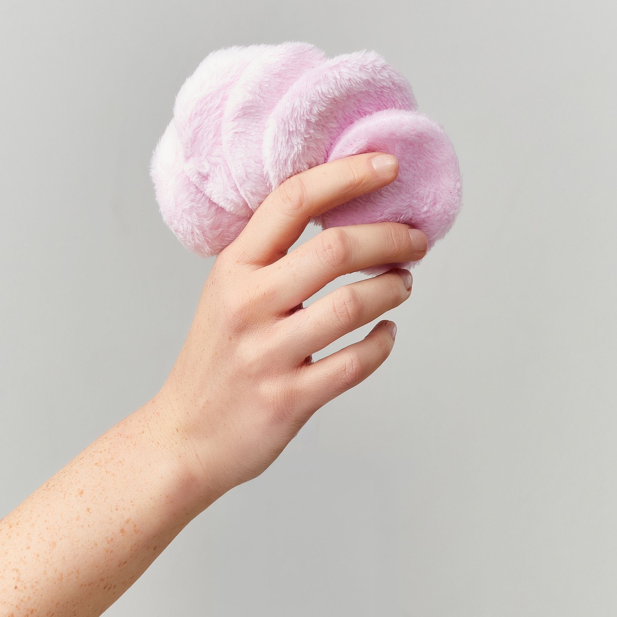 Hand hält mehrere runde rosa Wattepads.