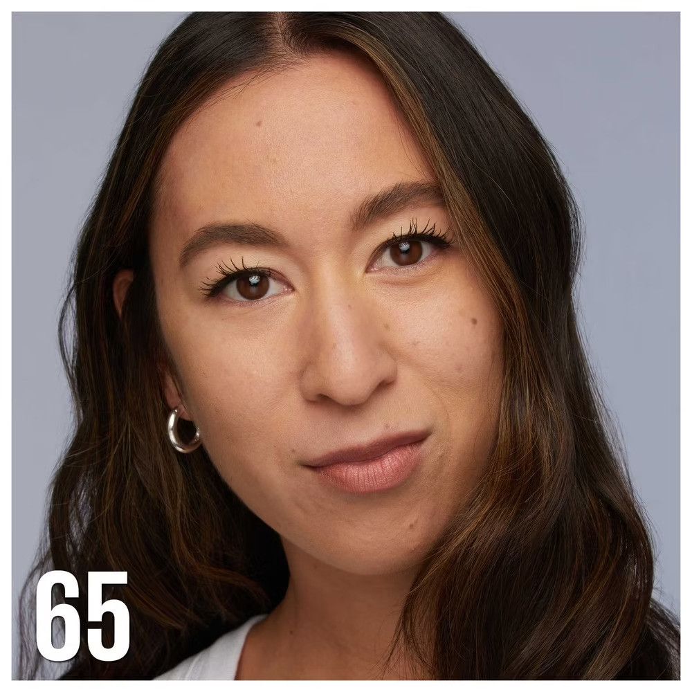 Porträt einer Frau mit gebräunter Haut. Sie trägt einen silbernen Ohrring. Auf dem Bild steht die Zahl 65.
