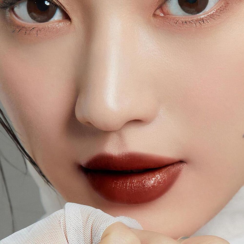 Nahaufnahme von Lippen mit braunem Lipgloss. Hautton, Augenbrauen und Augen sichtbar. Weiße Kleidung.
