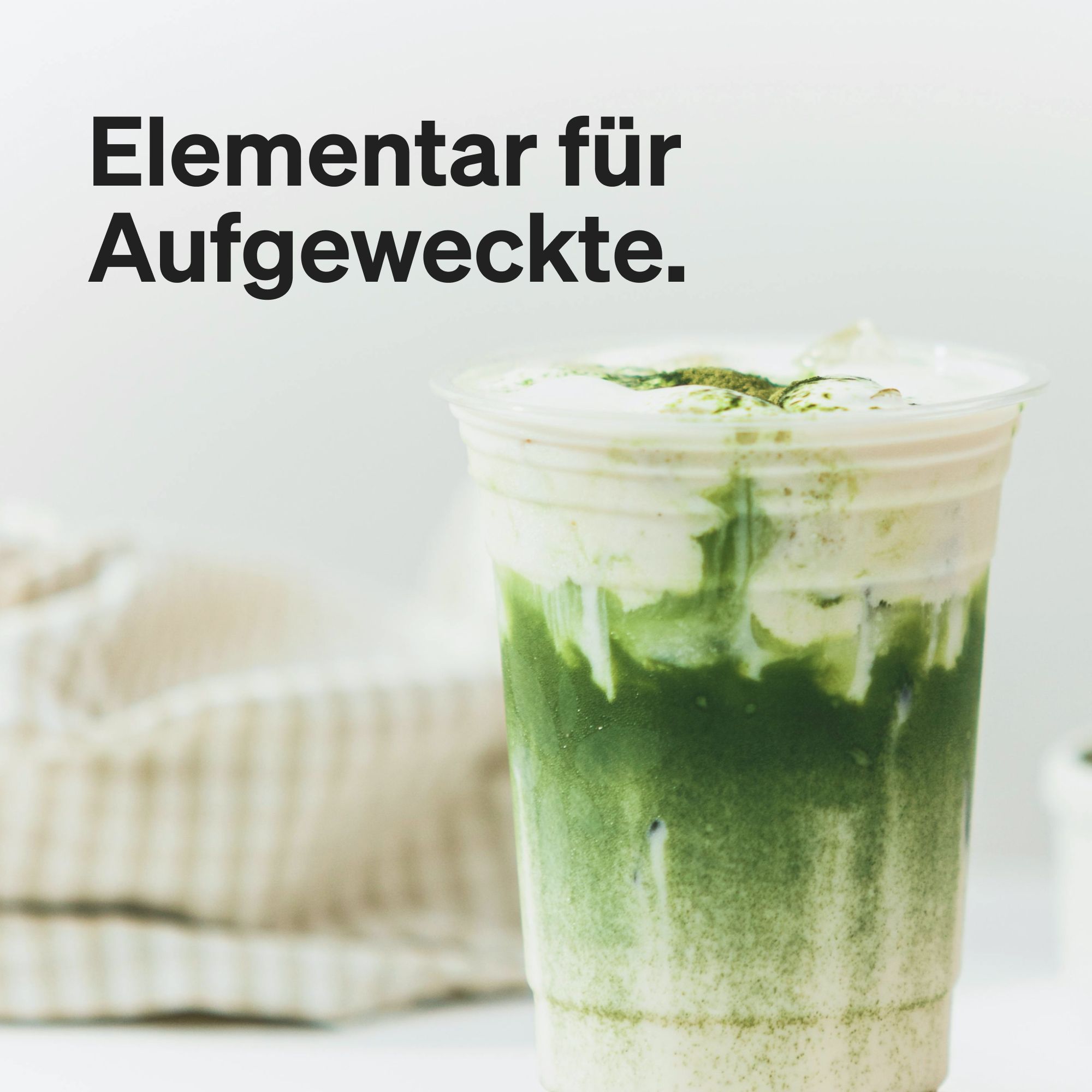 Glasbecher mit grünem Matcha-Getränk. Cremige Schicht oben. Text: Elementar für Aufgeweckte.