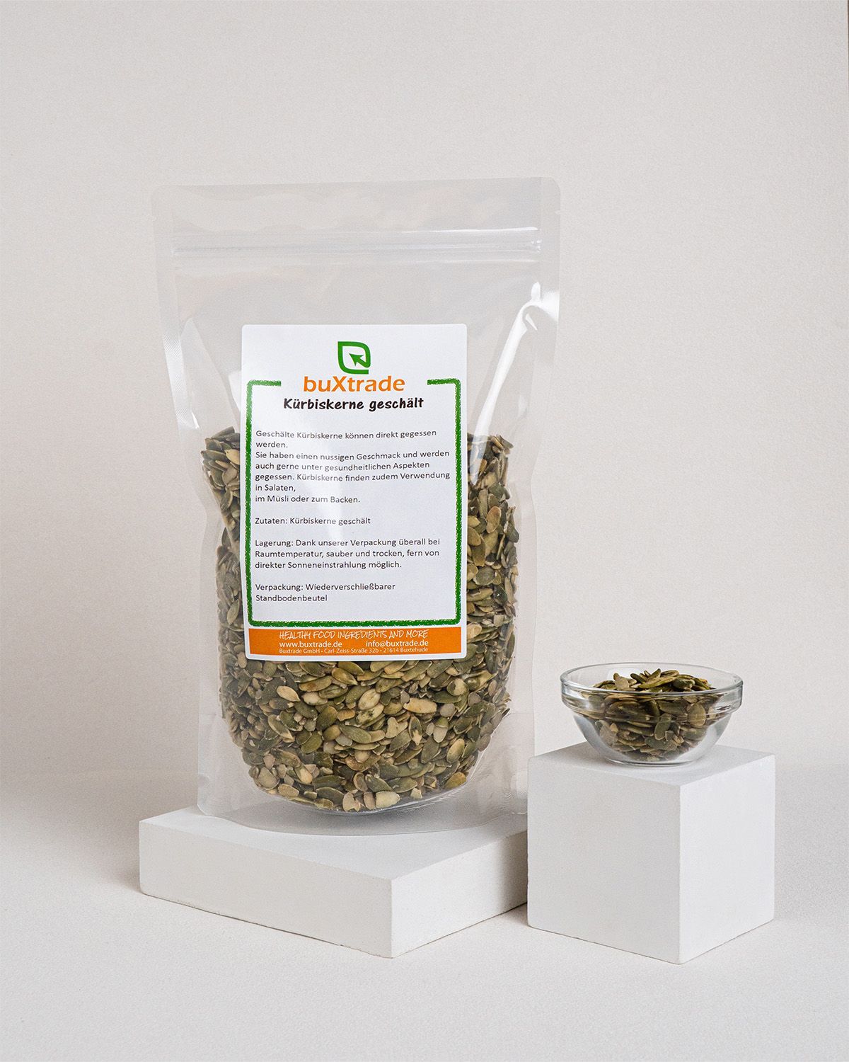 Verpackung mit Kürbiskernen und Glaschale auf Würfeln. Logo 'buXtrade' sichtbar. Helle Umgebung.