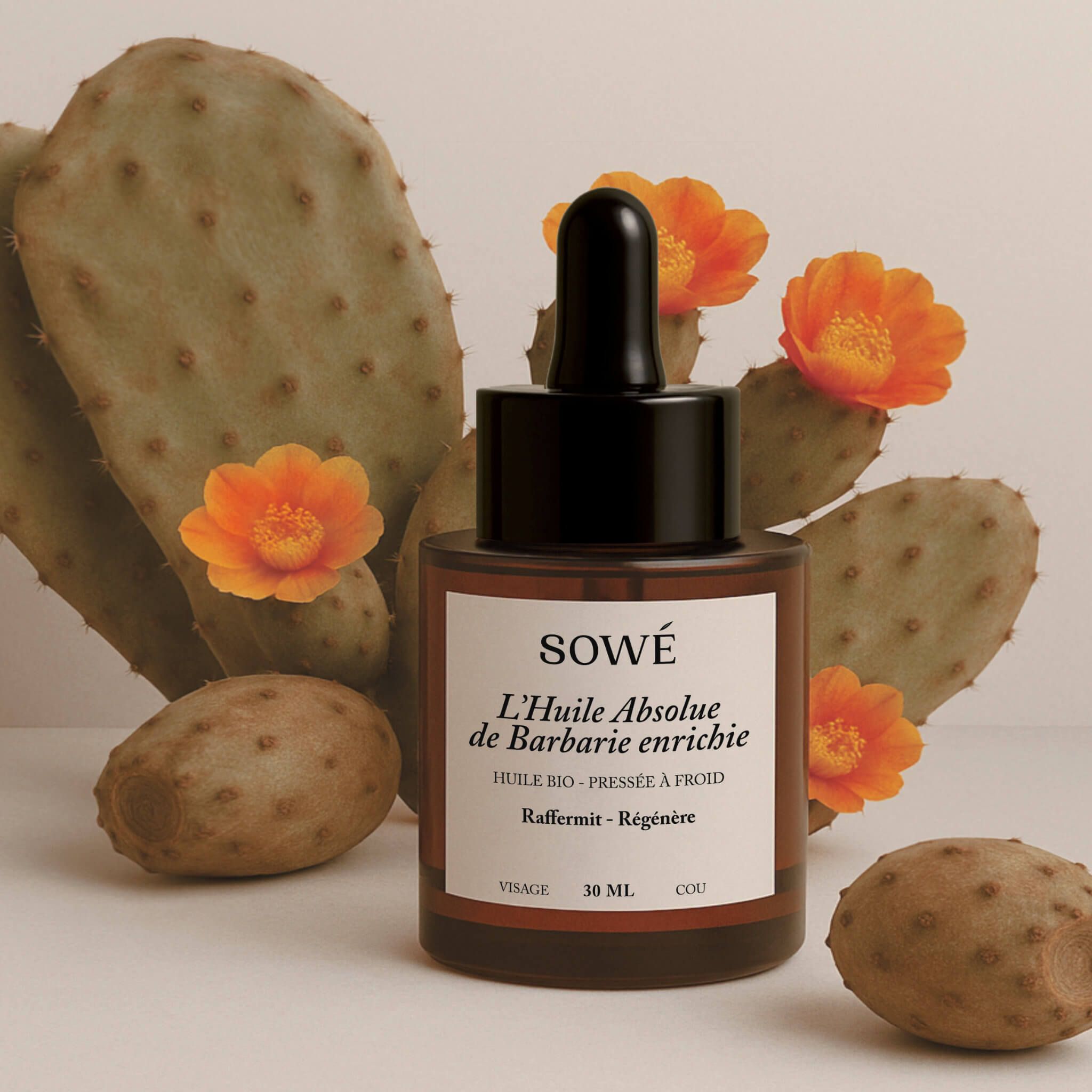 Braune Glasflasche mit Pipette, umgeben von Kaktusfeigen und Blüten. Etikett mit Text: SOWÉ, L'Huile Absolue.