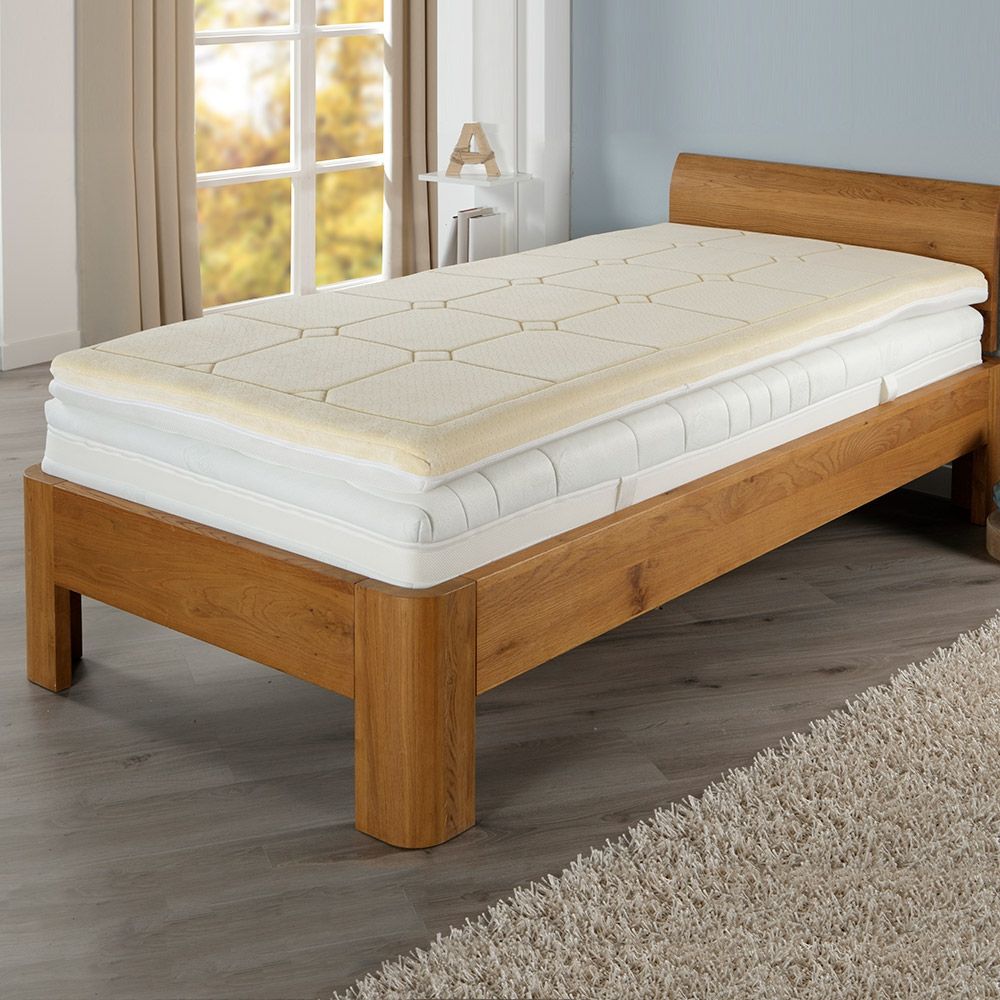 Bett mit Matratze und beiger Matratzenauflage.