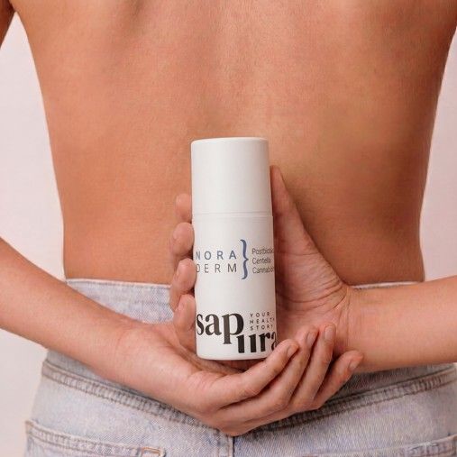 Weiße Spenderflasche mit 'Nora Derm' und 'SAPURA' Logo, gehalten hinter dem Rücken einer Person.