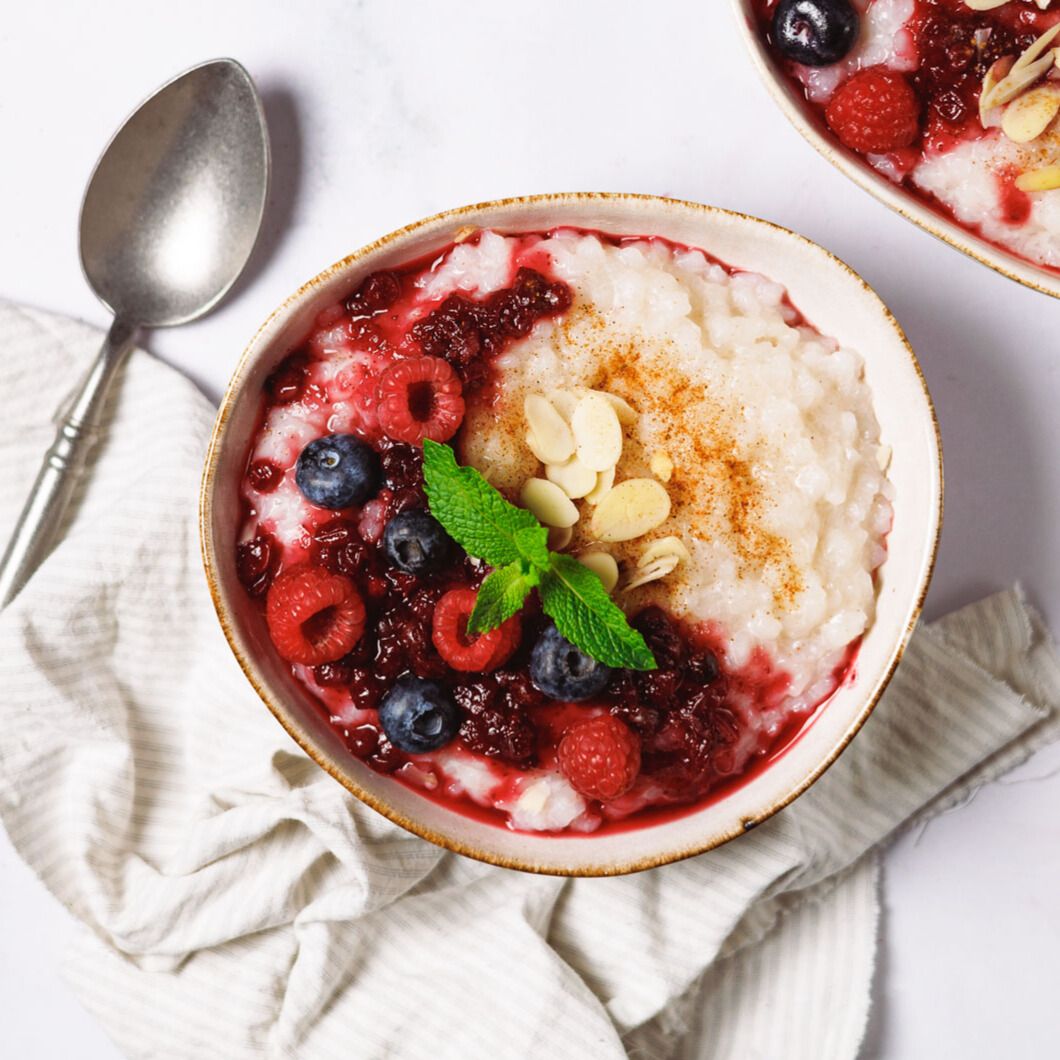Schüssel mit Reis, Beeren und Mandelsplittern. Garniert mit Minze. Auf weißem Untergrund.
