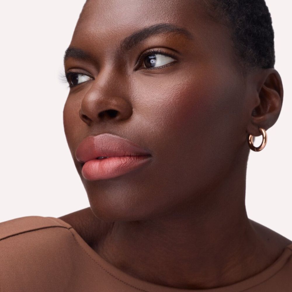 Porträt einer Frau mit rosafarbenem Lippenstift. Sie trägt goldene Creolen.