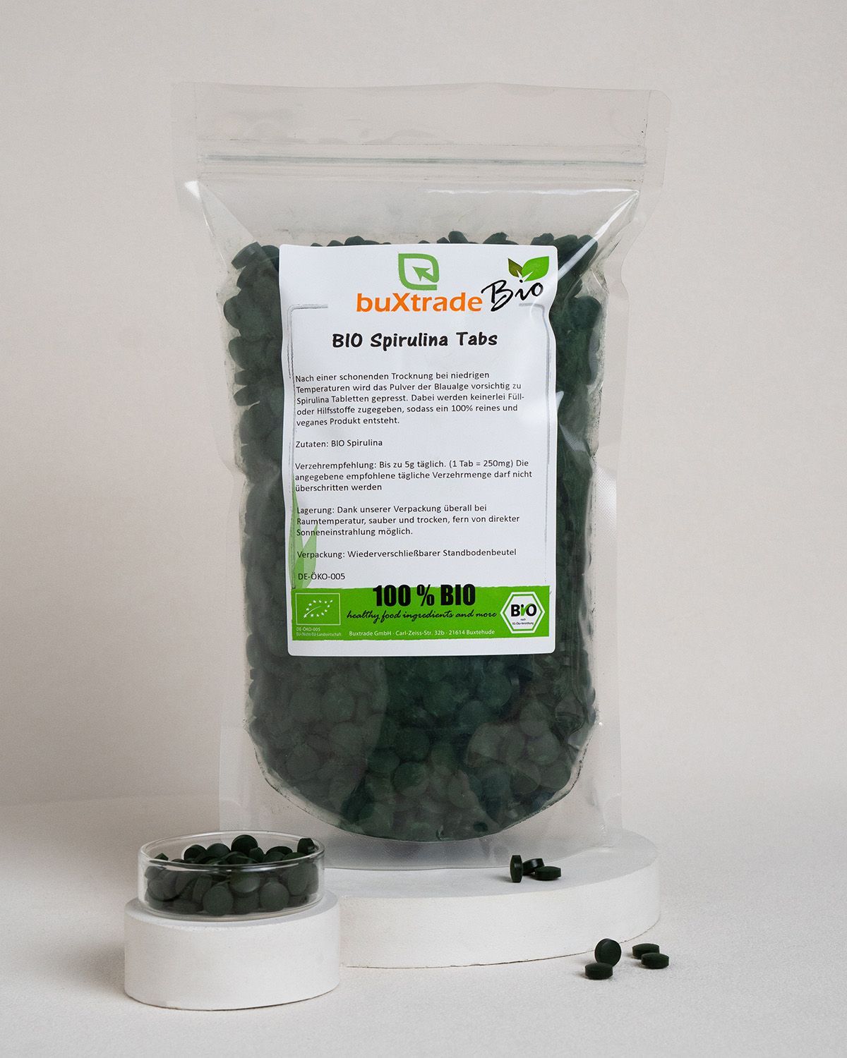 Plastiktüte mit Tabletten, Etikett: buXtrade Bio Spirulina Tabs. 100% BIO. Kleine Schale mit Tabletten daneben.