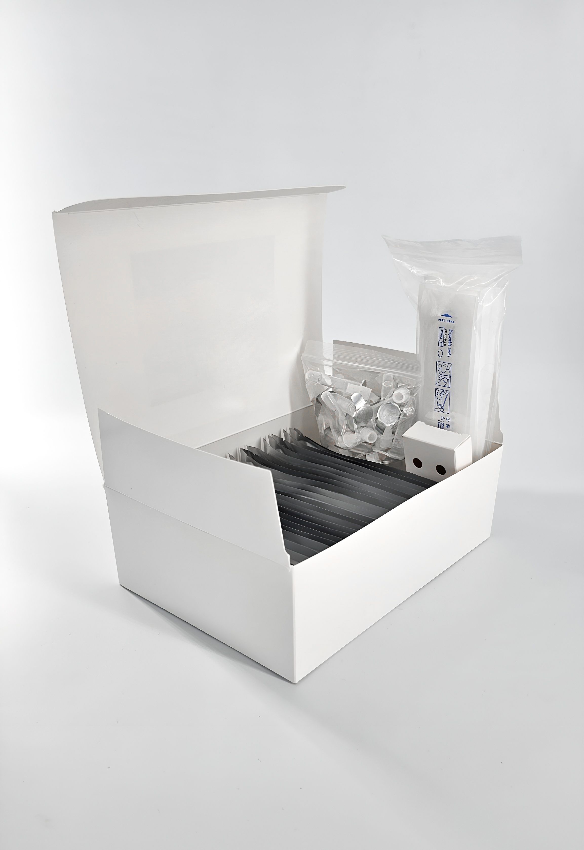 Geöffnete weiße Box mit Teststäbchen, Reagenzgläsern und Zubehör. Einzelne Komponenten in Plastik verpackt.